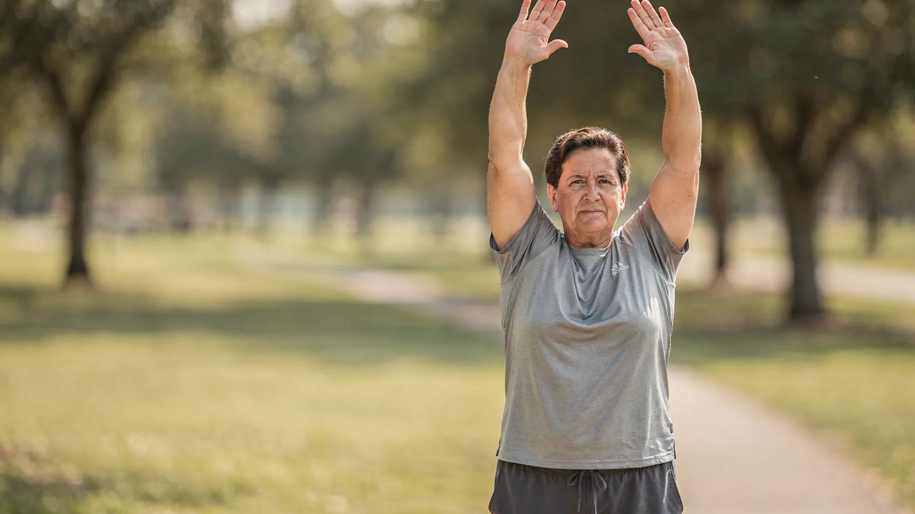 An adult approximately 30 to 45 years old stretching arms overhead after a light outdoor workout session